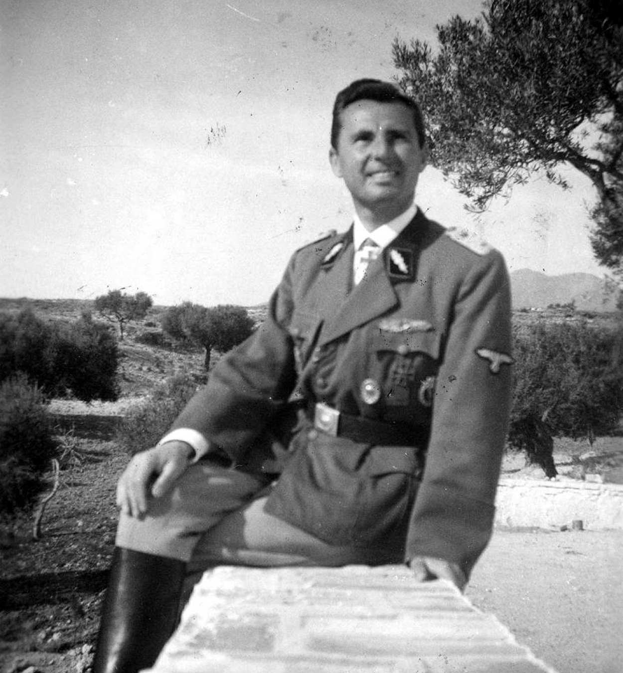 Léon Degrelle en uniforme Waffen-SS, assis en extérieur sur un muret