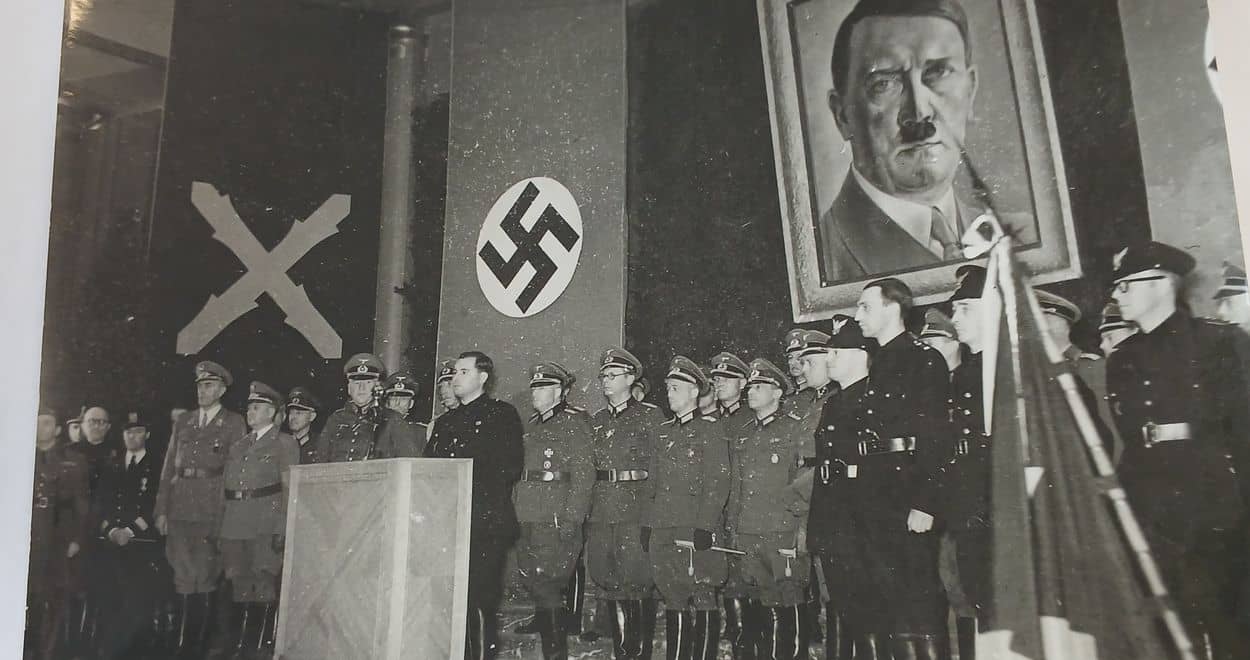 Léon Degrelle à la tribune, drapeaux rexiste et nazi, portrait d'Hitler